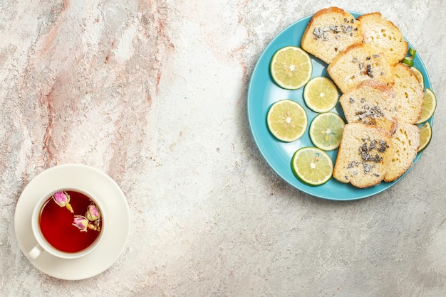 Draufsicht vom Teller mit einer Tasse Tee weiße Tasse schwarzen Tee auf der Untertasse neben dem blauen Teller des Kuchens und in Scheiben geschnittene Limette auf dem Tisch