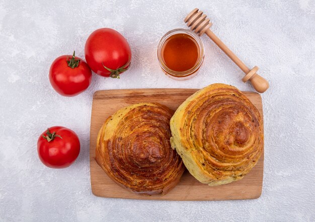 Draufsicht von aserbaidschanischem traditionellem gebäck gogal auf einem hölzernen küchenbrett mit honig auf einem glasglas mit frischen tomaten lokalisiert auf einem weißen hintergrund