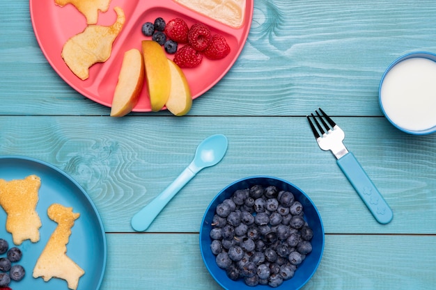 Draufsicht von Blaubeeren und Babynahrung auf Teller mit Besteck