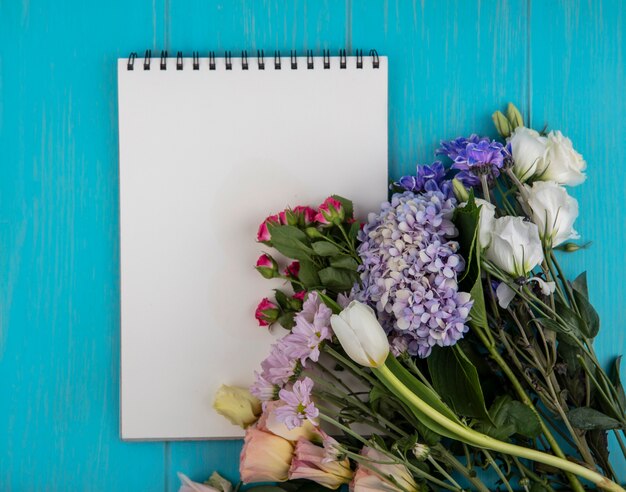 Draufsicht von Blumen und Notizblock auf blauem Hintergrund mit Kopienraum