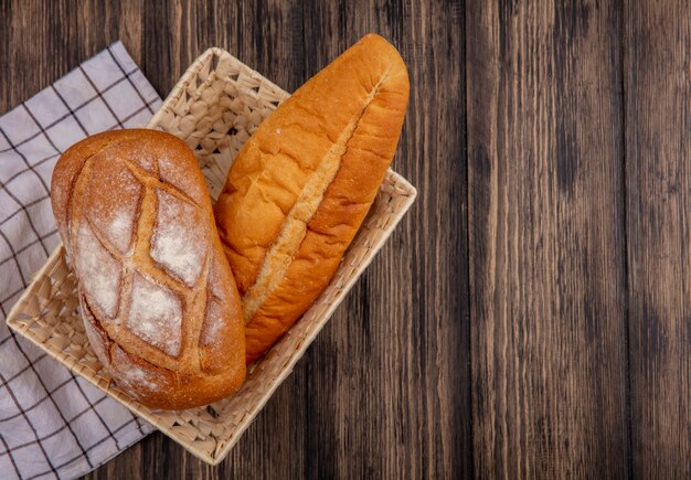 Draufsicht von Broten als knuspriges und vietnamesisches Baguette im Korb auf kariertem Stoff auf hölzernem Hintergrund mit Kopienraum