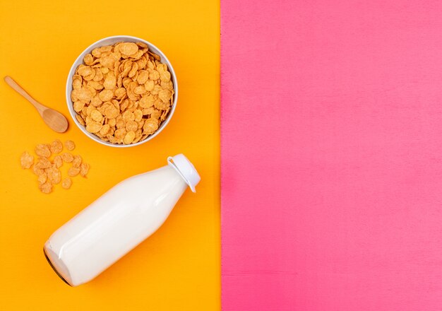 Draufsicht von Cornflakes und Milch mit Kopienraum auf rosa und gelbem Hintergrund horizontal