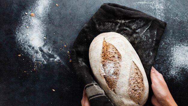 Draufsicht von den Händen, die ein Brot im Stoff halten