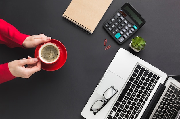 Draufsicht von den Händen, die Kaffeetasse auf Arbeitsschreibtisch halten