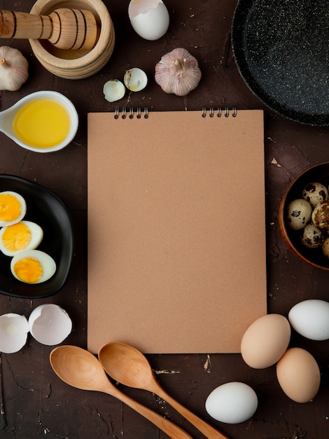 Draufsicht von Eiern und Butter mit Knoblauch und Löffeln auf kastanienbraunem Hintergrund mit Kopienraum