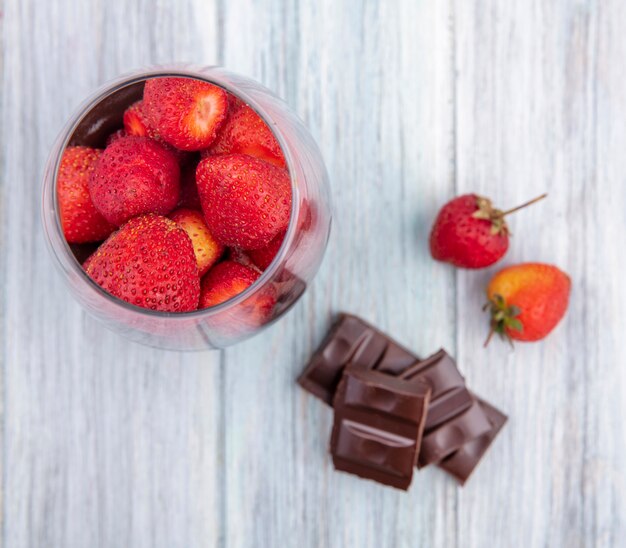 Draufsicht von Erdbeeren auf einem Glas mit Schokoriegel auf grauer Oberfläche