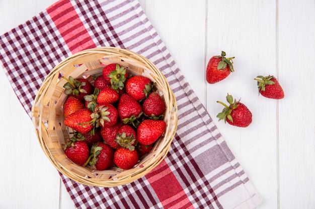 Draufsicht von Erdbeeren im Korb auf kariertem Stoff und auf Holzoberfläche
