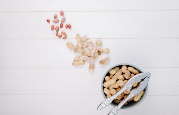 Draufsicht von Erdnüssen in einer Schüssel mit Nussknacker auf weißem Hintergrund