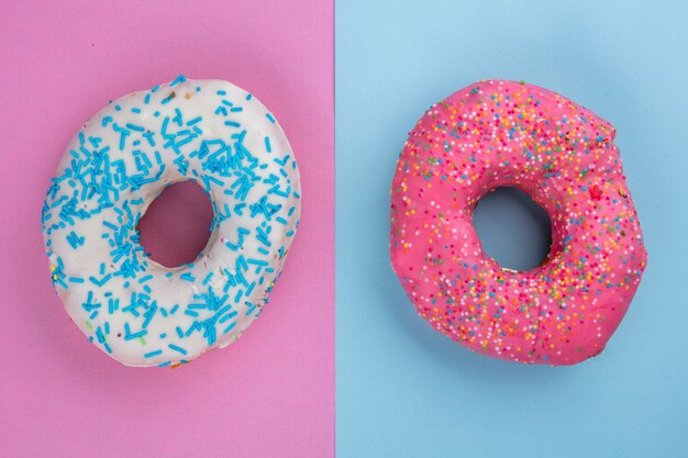 Draufsicht von farbigen süßen Donuts auf einer hellblau-rosa Oberfläche