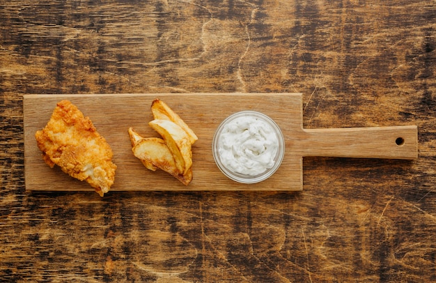 Draufsicht von Fisch und Chips auf Schneidebrett mit Soße