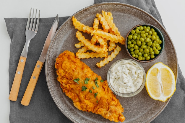 Draufsicht von Fish and Chips auf Teller mit Erbsen und Zitronenscheibe