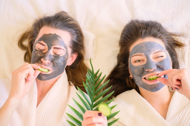 Draufsicht von Frauen mit Gesichtsmasken, die Gurkenscheiben essen