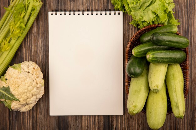 Draufsicht von frischem Gemüse wie Zucchini und Gurken auf einem Eimer mit Salat Blumenkohl und Sellerie isoliert auf einer Holzwand mit Kopierraum