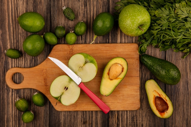 Draufsicht von frischen Avocados mit Äpfeln auf einem hölzernen Küchenbrett mit Messer mit Limettenfeijoas und Avocados lokalisiert auf einer Holzoberfläche