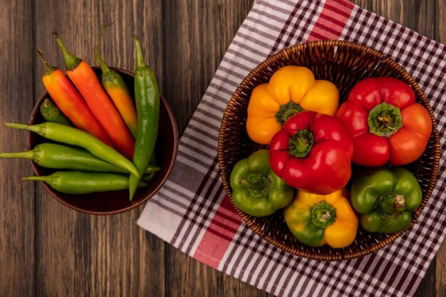 Draufsicht von frischen bunten Paprika auf einem Eimer auf einem karierten Tuch mit lang geformten grünen Paprika auf einer Schüssel auf einer Holzoberfläche