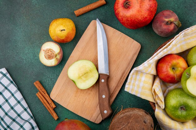 Draufsicht von frischen Früchten wie Apfel auf Holzküchenbrett mit Messerpfirsich-Granatapfelbirne und Zimtstangen auf Grün