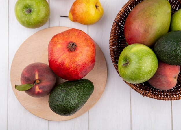 Draufsicht von frischen Früchten wie Pfirsichgranatapfel auf Holzküchenbrett mit einem Eimer von Früchten und Apfelpfirsichen lokalisiert auf Weiß