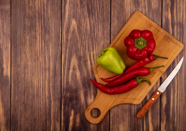 Draufsicht von frischen Glocken- und Chilischoten auf einem hölzernen Küchenbrett mit Messer auf einer Holzwand mit Kopierraum