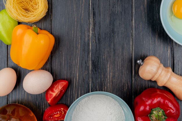 Draufsicht von frischen Hühnereiern mit einer Tomatenscheibe mit bunten Paprikaschoten auf einem hölzernen Hintergrund mit Kopienraum