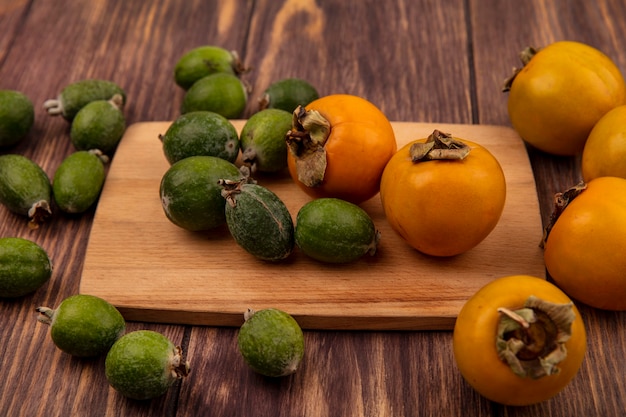 Kostenloses Foto draufsicht von frischen orangenkakifrüchten mit feijoas auf einem hölzernen küchenbrett auf einer hölzernen oberfläche