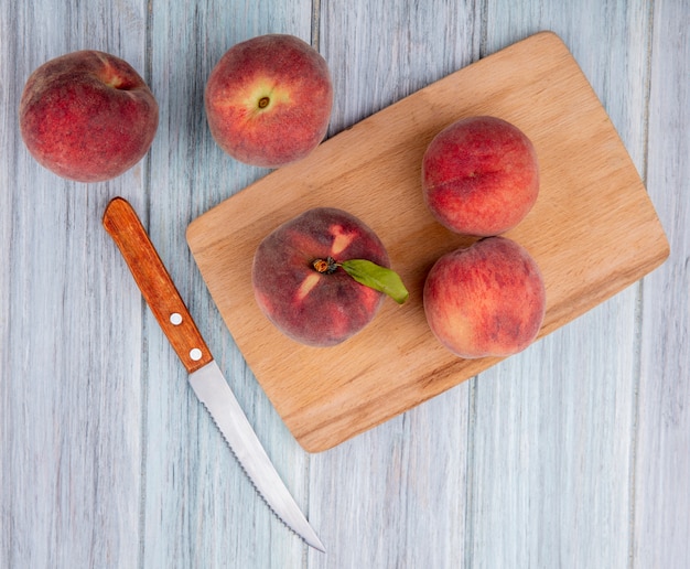 Draufsicht von frischen Pfirsichen und Küchenmesser auf Holzküchenbrett auf Grau