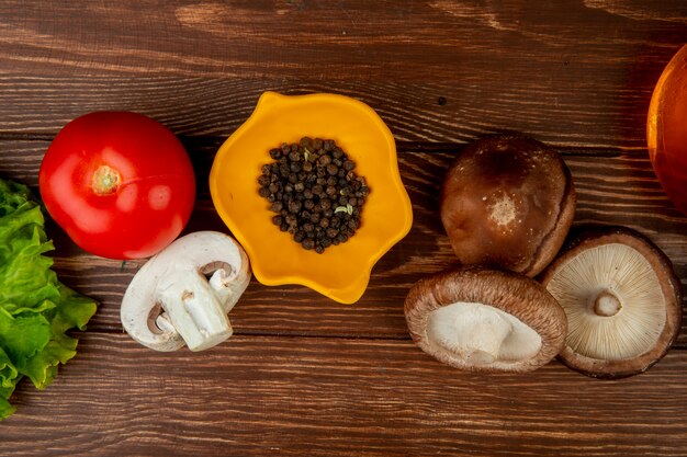 Draufsicht von frischen Pilzen und schwarzen Pfefferkörnern mit Tomate auf rustikalem Holz