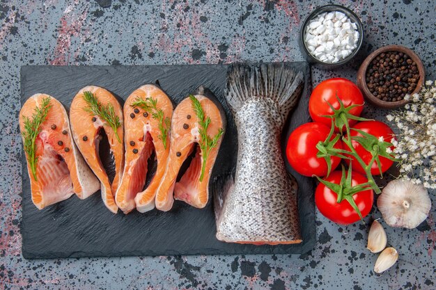 Draufsicht von frischen rohen Fischgrüns auf dunklen Farbschalengewürztomaten mit Stielen Knoblauchblumen auf blau schwarzer Mischfarbtabelle