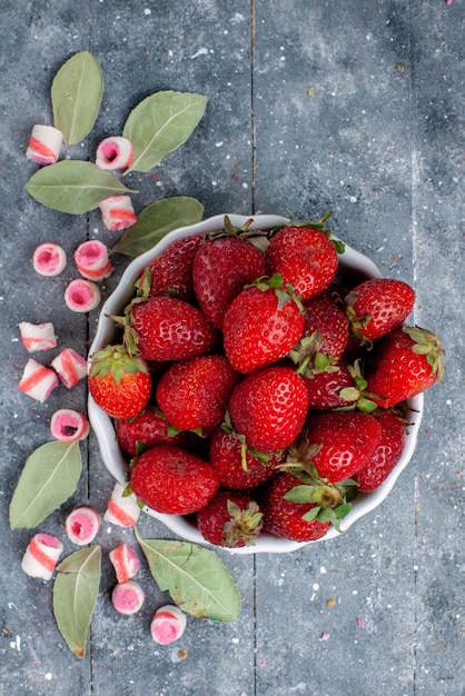 Kostenloses Foto draufsicht von frischen roten erdbeeren innerhalb platte zusammen mit geschnittenen rosa bonbons auf grauem, frischem beerenfruchtbeere