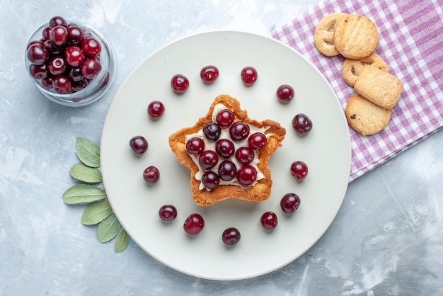 Draufsicht von frischen sauerkirschen innerhalb platte mit sternförmigem cremigem kuchen und keksen auf weißem, fruchtigem saurem sommerkuchenplätzchen