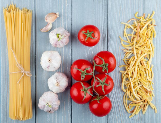 Draufsicht von frischen Tomaten mit Knoblauch und rohen Nudeln mit Spaghetti auf Holz rustikal