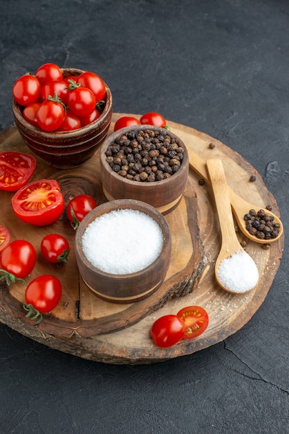 Draufsicht von frischen Tomaten und Gewürzen in Schalenlöffeln auf Holzbrett auf schwarzer Oberfläche