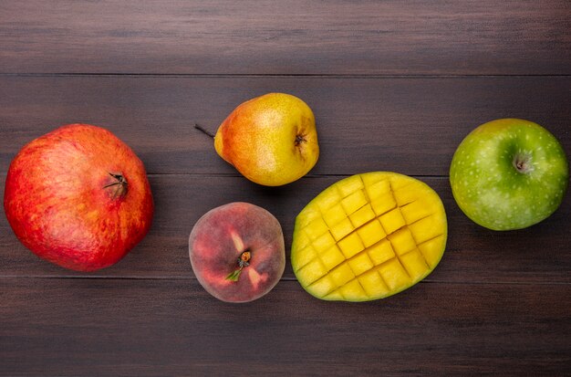 Draufsicht von frischen und bunten Früchten wie Granatapfel geschnittenem Mangobirnenpfirsichapfel auf Holz