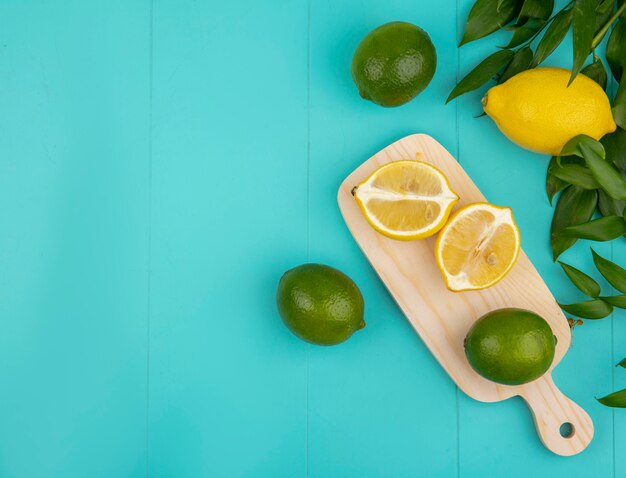 Draufsicht von frischen und bunten Zitronen mit grünen Blättern auf hölzernem Küchenbrett auf Blau