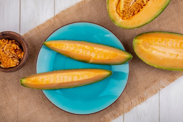 Draufsicht von frischen und köstlichen Melonenscheiben auf blauem Teller auf Sackleinen auf Weiß