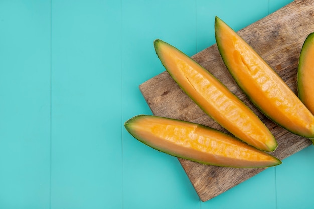 Draufsicht von frischen und köstlichen Melonenscheiben der Kantalupe auf hölzernem Küchenbrett auf Blau