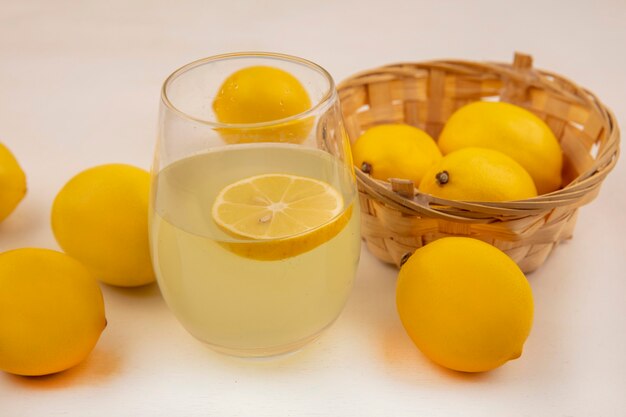 Draufsicht von frischen Zitronen auf einem Eimer mit frischem Zitronensaft in einem Glas auf einer weißen Wand