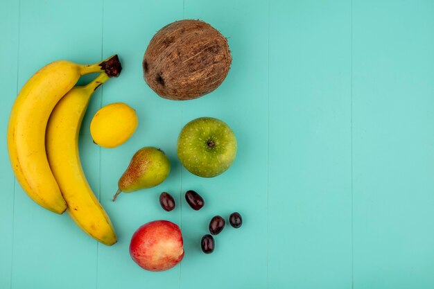 Draufsicht von Früchten als Bananenapfel-Zitronenpfirsich-Traubenbeeren-Birnenkokosnuss auf blauem Hintergrund mit Kopienraum