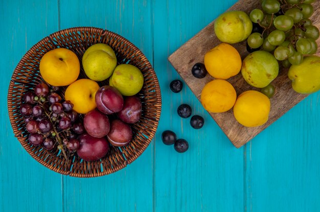 Draufsicht von Früchten als Nectacots pluots Traube im Korb und auf Schneidebrett mit Traubenbeeren auf blauem Hintergrund