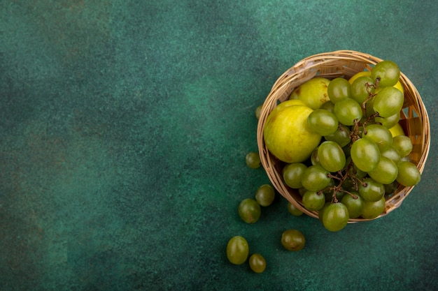 Draufsicht von Früchten als Traube und Pluot im Korb auf grünem Hintergrund mit Kopienraum