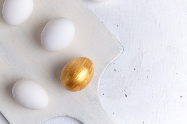 Draufsicht von ganzen eiern mit goldenem ei auf der weißen oberfläche