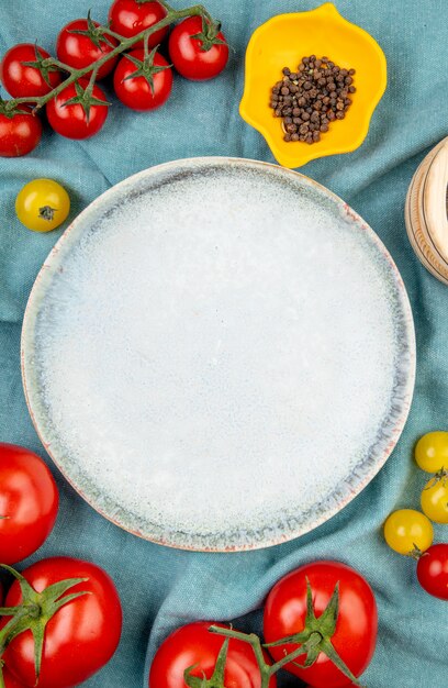 Draufsicht von gelben und roten Tomaten mit schwarzen Pfeffersamen auf blauem Stofftisch