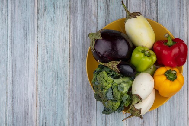 Draufsicht von Gemüse als Pfefferbrokkoli und Aubergine in Platte auf hölzernem Hintergrund mit Kopienraum