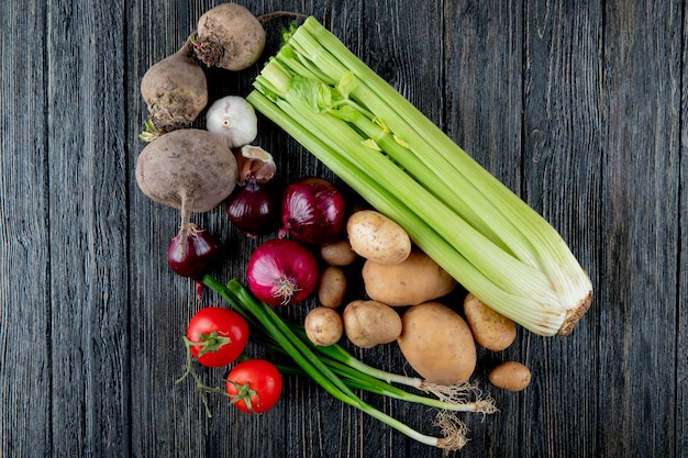 Draufsicht von Gemüse als Sellerie-Rote-Bete-Knoblauch-Zwiebel-Tomate und Frühlingszwiebel auf hölzernem Hintergrund mit Kopienraum