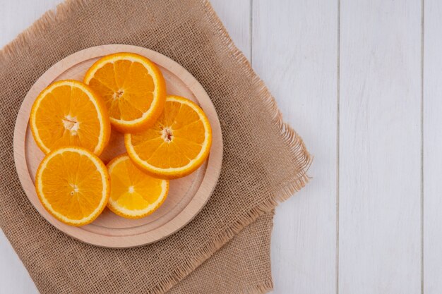 Draufsicht von geschnittenem Orange auf einem Ständer auf einer beigen Serviette auf einer weißen Oberfläche
