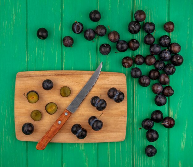 Draufsicht von geschnittenen und ganzen Schlehenbeeren mit Messer auf Schneidebrett und auf grünem Hintergrund