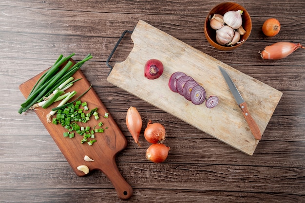 Draufsicht von geschnittenen Zwiebeln auf Schneidebrettern mit Knoblauch und Messer auf hölzernem Hintergrund