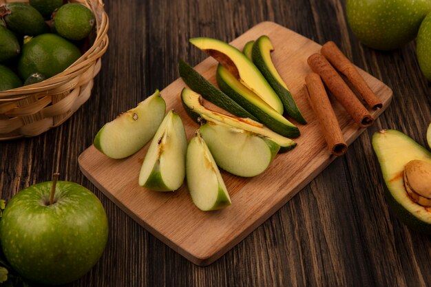 Draufsicht von gesunden gehackten Scheiben von Avocados auf einem hölzernen Küchenbrett mit Zimtstangen und Apfelscheiben mit Feijoas auf einer hölzernen Oberfläche