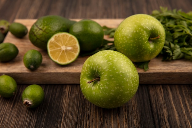 Draufsicht von gesunden grünen Äpfeln auf einem hölzernen Küchenbrett mit Feijoas-Limetten-Avocados und Petersilie lokalisiert auf einer Holzwand