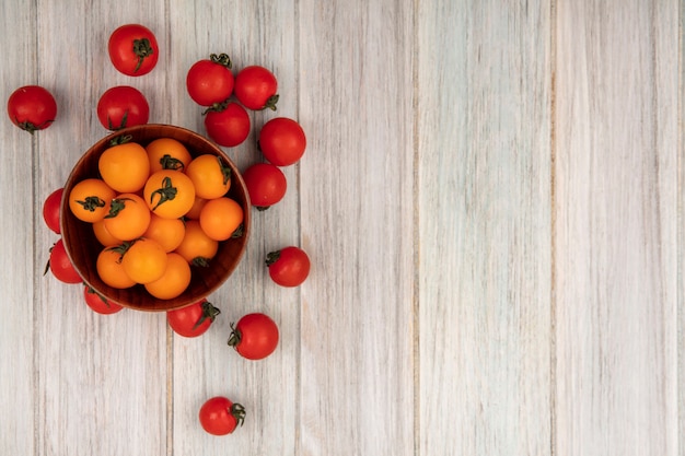 Draufsicht von gesunden orange Tomaten auf einer Holzschale mit roten Tomaten lokalisiert auf einer grauen Holzoberfläche mit Kopienraum