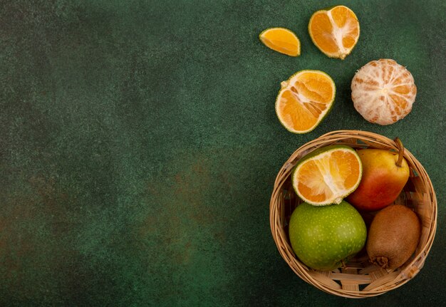 Draufsicht von gesunden und frischen Früchten wie Apfel-Birnen-Kiwi auf einem Eimer mit Mandarinen, die mit Kopienraum isoliert werden
